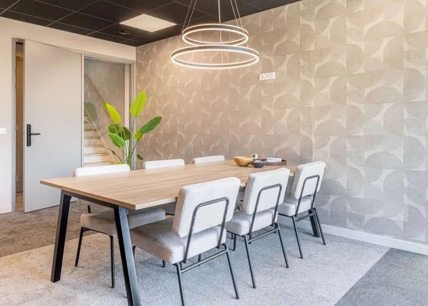 A bright meeting room with a wooden table, white chairs and a round lamp.