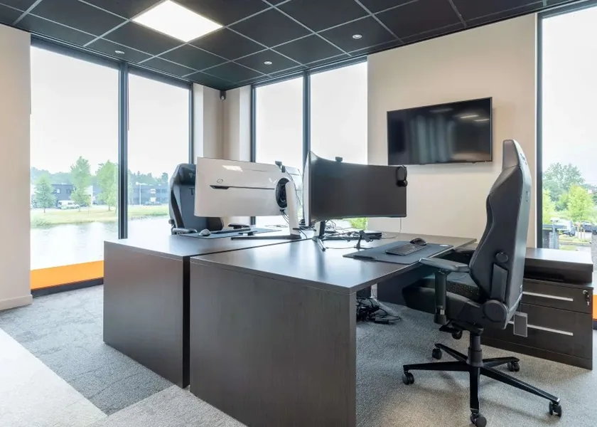 An office workspace with two desks, monitors and a view of the water.