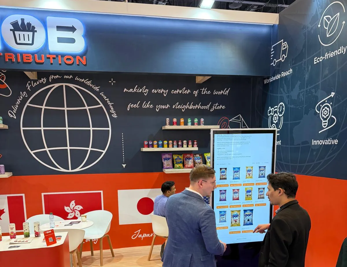 BOB Distribution's stand at a trade fair: a dark blue wall with a globe and the BOB logo, flags on an orange band and two visitors at a large touchscreen.